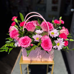 Pink roses and daisies arranged in a pink handled gift box