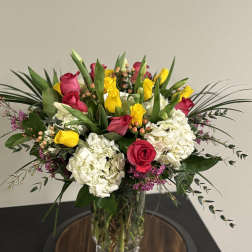 Bouquet of pink and yellow roses with white hydrangeas in a clear glass vase