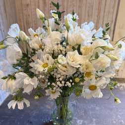 Tall glass vase of white daisylike blooms and lisianthus with yellow centers in a loose, airy arrangement