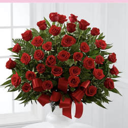 Large arrangement of red roses with red ribbon in a white pedestal vase