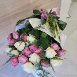 Bouquet of pink and cream roses wrapped in white paper with a satin ribbon bow