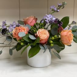 Peach roses and lavender flowers in a white vase