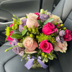 Bouquet of pink and lavender roses in a glass vase with a purple ribbon