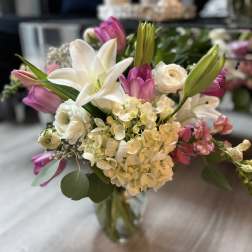 Mixed bouquet of white lilies, hydrangeas, and pink tulips in a clear glass vase