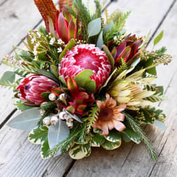 Bouquet of pink protea and mixed greenery on a wooden surface