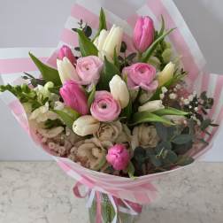 Pink and white mixed bouquet with tulips and ranunculus in striped wrap