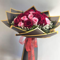 Bouquet of red and pink roses wrapped in black paper with a pink ribbon