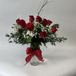 Red roses arranged in a glass vase with baby's breath and a red bow