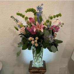 Tall mixed bouquet with pink lilies, roses, and blue flowers in a glass vase