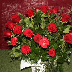 Arrangement of red roses with a few red carnations in a white basket against a burgundy background