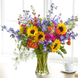 Colorful bouquet with sunflowers, roses, and purple flowers in a glass vase