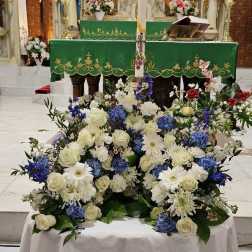 Low blue and white altar arrangement with roses and mums around a tall decorative candle