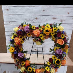 Heart-shaped floral wreath on a metal stand with roses and sunflowers