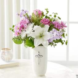 Pink and white flower arrangement in a white vase with a cross emblem