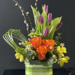 Orange roses and purple tulips in a striped glass vase