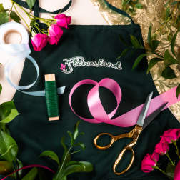 Floral design tools with pink roses, ribbon, scissors, and a dark apron