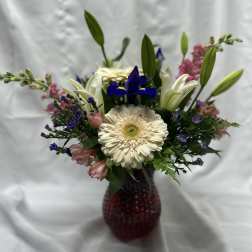 Mixed bouquet with a white gerbera daisy, lilies, and purple accents in a red vase