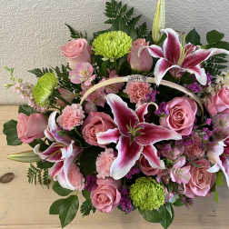 Pink roses and lilies arranged in a basket with green mums