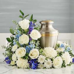 White roses and blue-purple flowers arranged around a metal urn