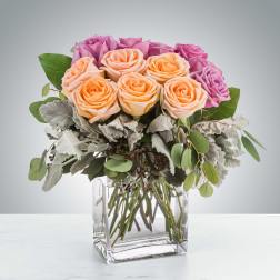 Low square vase of peach and purple roses with soft silvery foliage accents