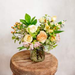 Cream and peach roses in a glass vase with small white flowers