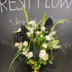 White floral arrangement with black feathers in a gold vase