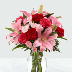 Pink lilies and red roses arranged in a clear glass vase