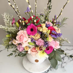 Colorful arrangement of pink gerberas, roses and mixed blooms in a white round vase with tall pussy willow branches