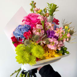 Bright hand-tied bouquet with pink roses, blue carnations, lime mums and assorted mixed blooms in white wrap