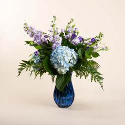 Blue hydrangeas and purple flowers in a blue glass vase