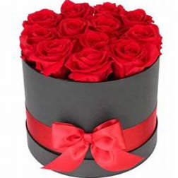 Red roses arranged in a round black box with a red ribbon bow