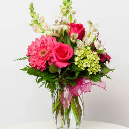 Pink roses and gerbera daisies in a glass vase with a pink ribbon