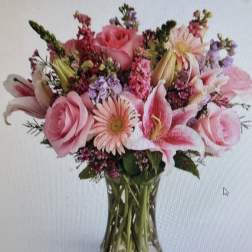 Pink roses, lilies, and gerbera daisies arranged in a clear glass vase