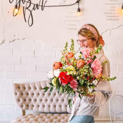 Woman holding a large mixed bouquet of pink, red, white, and peach flowers