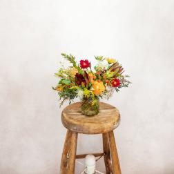 Mixed bouquet in a glass jar on a wooden stool