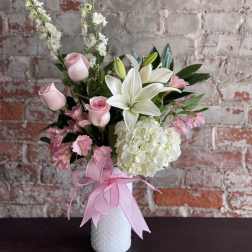 Pink roses and white lilies in a white vase with a pink ribbon