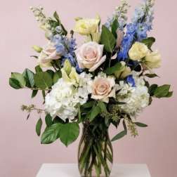 Mixed bouquet of pastel roses, hydrangeas, and blue delphinium in a glass vase
