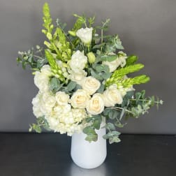 White roses and lisianthus in a white vase with green filler