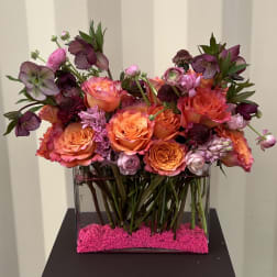 Mixed pink and orange flower arrangement in a clear rectangular vase