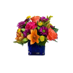 Colorful bouquet in a blue glass vase with roses, lilies, and daisies
