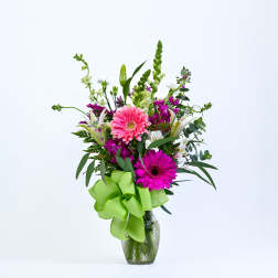 Pink and magenta gerbera bouquet in a glass vase with a green ribbon