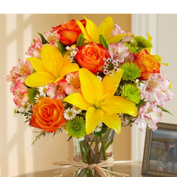 Mixed bouquet of yellow lilies, orange roses and pink flowers in a glass vase with a raffia bow