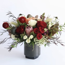 Arrangement of red and cream roses with protea and other blooms in a dark gray vase