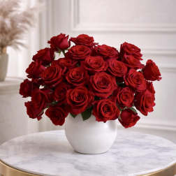 Low white vase filled with many red roses on a round marble table