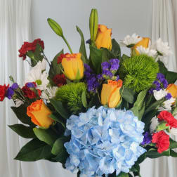 Colorful bouquet with blue hydrangea, roses, carnations, and daisies in a blue vase