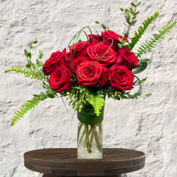 Red roses arranged in a clear glass vase with greenery