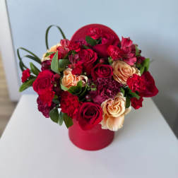 Red and peach roses arranged in a round red box