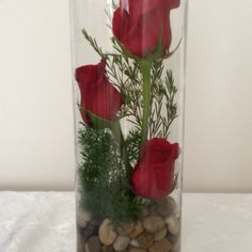 Three red roses in a tall glass vase with pebbles