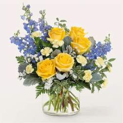 Yellow roses and blue flowers arranged in a clear glass vase