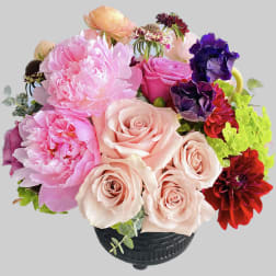 Mixed bouquet of pink roses, peonies, and purple blooms in a black vase